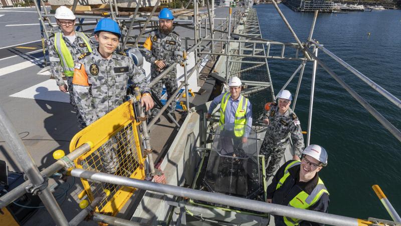Fleet Support Unit sailors and officers with BAE Systems staff surround the upgraded Advanced Stabilised Glide Slope Indicator on HMAS Adelaide's flight deck. Photo: Leading Seaman Jarrod Mulvihill