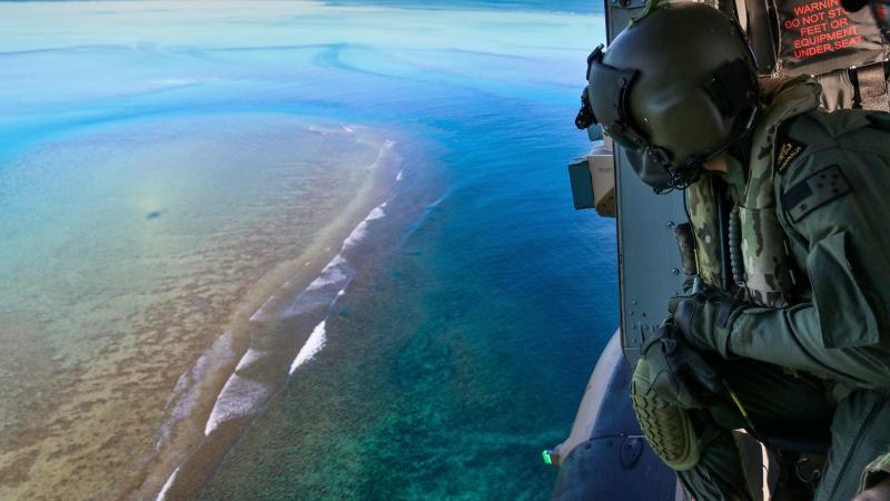 Leading Seaman Daniel Atkins looks out over Elizabeth Reef searching for unexploded ordnance from a MRH-90 helicopter. Photo: Sergeant Jake Sims