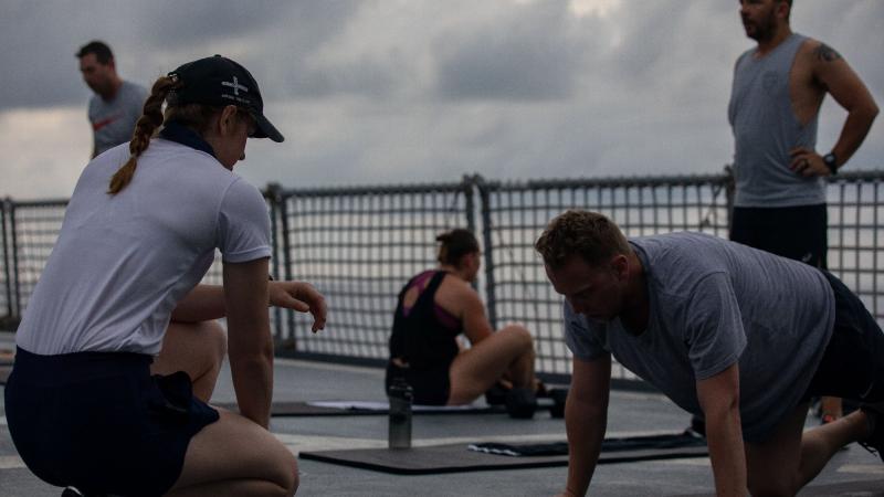 Physical Training Instructor Jamie Lord, left, instructs an early morning fitness class on HMAS Ballarat's flight deck while en route to Exercise Malabar. Photo: Leading Seaman Shane Cameron