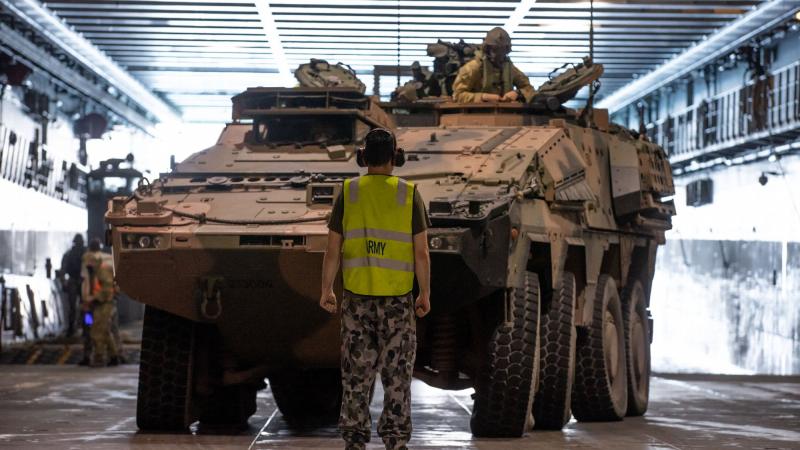 A soldier guides a Boxer Combat Reconnaissance Vehicle into position on HMAS Adelaide. Photo: Trooper Jonathan Goedhart