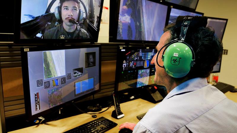 Simulator Pilot Instructor Ben Scorey, of Canadian Aviation Electronics, monitors and instructs Pilot Officer Alec Taylor in the Hawk 127 Simulator during a trial of eye tracking technology. Photo: Corporal Brett Sherriff
