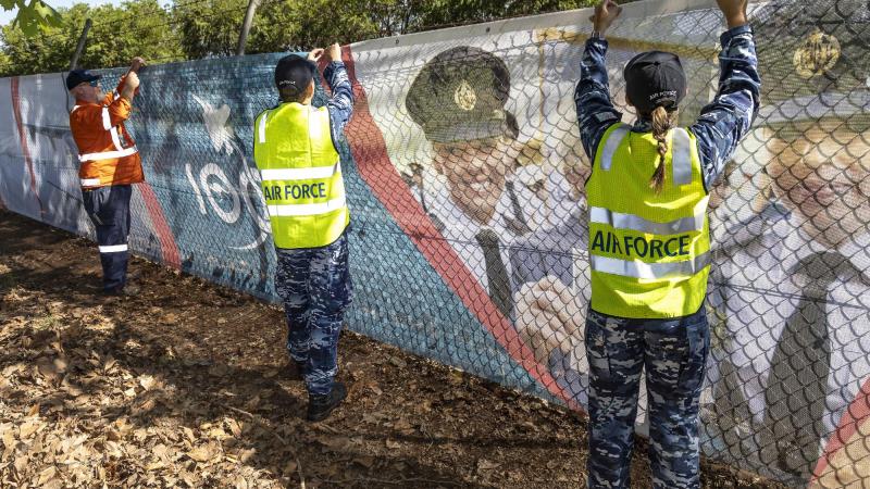 Leading Aircraftman Nathan Palmer, centre, and Aircraftwoman Alanna Hennessy both from No. 22 Squadron, assist BGIS employee Michael Gavin instal an Air Force 2021 banner. Photo: Corporal Dan Pinhorn