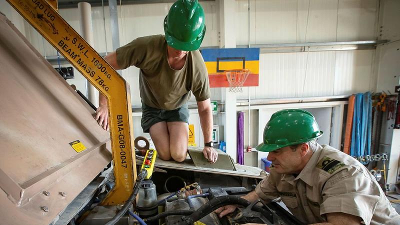 Lance Corporal Cameron Pennell, left, and Rear Admiral Michael Rothwell begin removing the engine from a protected mobility vehicle in the Middle East region. Photo: Sergeant Ben Dempster