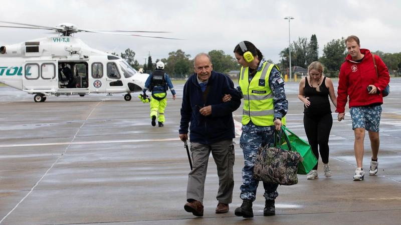 Leading Aircraftwoman Leah McDonald helps evacuee Ian Clucas across the tarmac at RAAF Base Richmond. Photo: Corporal Kylie Gibson
