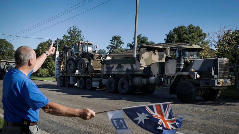 Darcy Elbourne waves the Australian flag in the driveway of his home as Army personnel head out to conduct relief and recovery tasks during Operation NSW Flood Assist in Taree. Photo: Corporal Sagi Biderman
