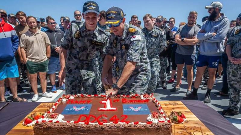 HMAS Sydney's youngest crew member Seaman Sebastien Schultz, left,  and Commanding Officer Commander Edward Seymour cut a cake to mark the first anniversary of the ship's commissioning into the Navy.