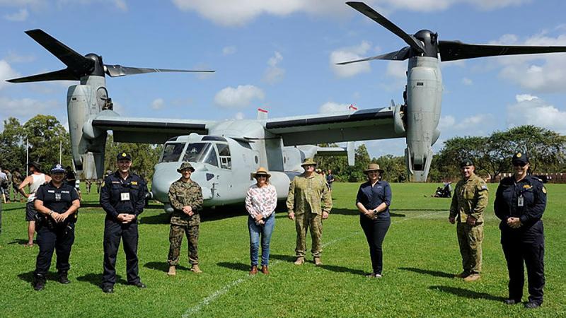 Community leaders and representatives from the NT Police and Australian Border Force stand with ADF and US Marine Corps members in front of an MV-22B Osprey.