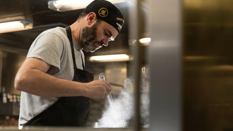 Commanding Officer HMAS Brisbane Commander Aaron Cox, cooks 'midnighters' for his crew in the galley, during Exercise Talisman Sabre. Photo: Leading Seaman Daniel Goodman