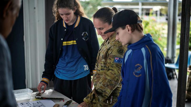 Warrant Officer Class One Kelly Hammant instructs students from Redbank Plains State High School how to paint boomerangs in traditional styles. Photo: Private Jacob Hilton 