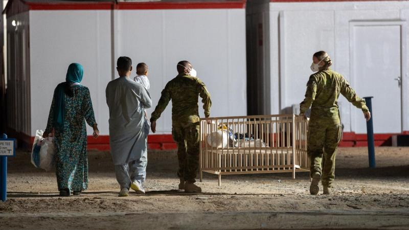 Signaller Charbal Nunes, of 145 Signal Squadron, and Corporal Nikkiska McGlashan, of 3 Combat Signal Regiment, help a family transport a cot to their room at the temporary camp in Australia’s main operating base in the Middle East. 
