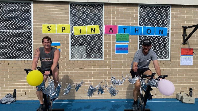 Petty Officer Simon Taylor, left, and Lieutenant Commander James Knight compete in the HMAS Watson spin-a-thon fundraiser for Dry July.