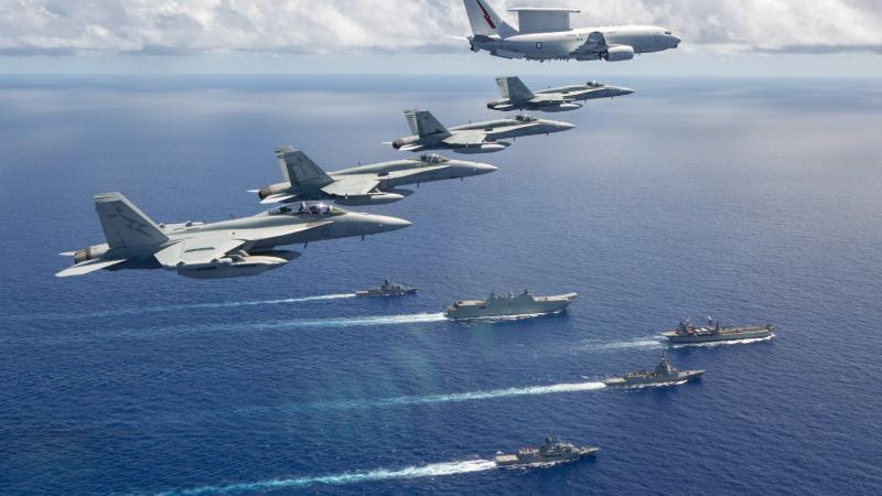A formation from Air Force of an E-7A Wedgetail, three F/A-18A Hornets, and an EA-18G Growler from fly over a Navy task group of HMA Ships Canberra, Hobart, Stuart, Arunta and Sirius during the Regional Presence Deployment in July 2020. 
