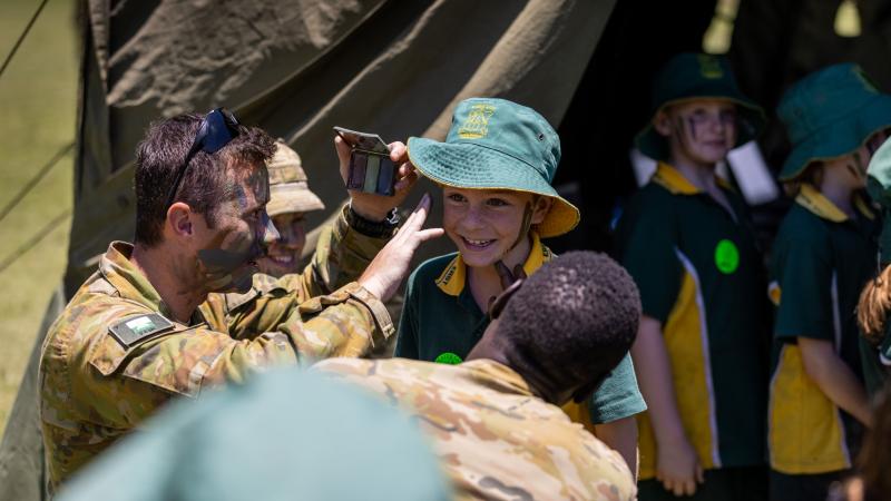 Soldiers from the 7th Combat Signal Regiment apply camouflage cream to a student at Gympie East State School. Photo: Patrick Maher