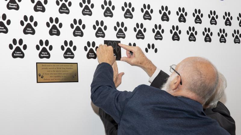 RAAF Dog Handlers Association members Ray Thomas, right, and Kim Hodgeo add another member's name to the RAAF Dog Handlers Association wall of remembrance at the RAAF Security and Fire School, RAAF Base Amberley. Photo: Leading Aircraftwoman Emma Schwenke