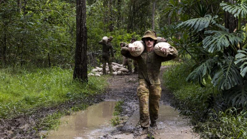 An Army officer from 7th Brigade carries sandbags across a flooded section of trail to repair flood-damaged access tracks in Imbil, Queensland, as part of Operation Flood Assist 2022. Photo: Corporal Julia Whitwell