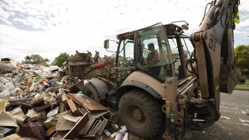 An Army soldier uses a backhoe to clear flood-damaged household goods from a street in Lismore, as part of Operation Flood Assist 2022. Photo: Warrant Officer Class Two Max Bree