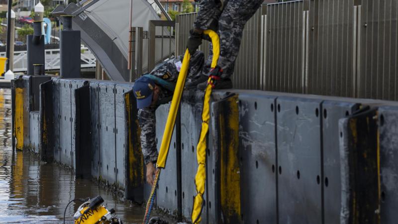 Navy divers Chief Petty Officer Cameron Schmid, right, and Able Seaman Jordan Bitolkoski, centre, assist Able Seaman Jake Phillips as he surveys ferry terminals pylons along the Brisbane River. Photo: Corporal Julia Whitwell