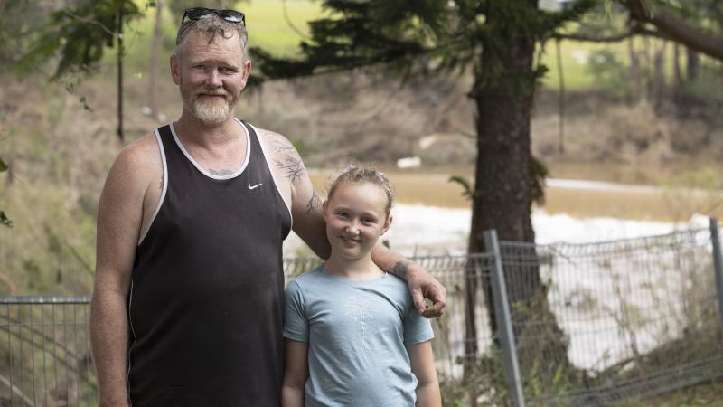 Casino local Terry Lloyd with his youngest daughter stand in his daughter Clarisa's Casino, New South Wales, backyard with the Richmond River, which flooded the house, in the background. Photo: Corporal Sagi Biderman