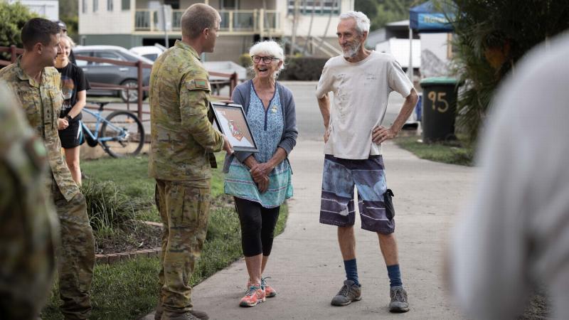 Australian Army officer Lieutenant Brook Wright (centre left) from 8th/9th Battalion, Royal Australian Regiment, presents Broadwater, locals Annette and Trevor Walsh with a unit flag. Photo: Corporal Jonathan Goedhart