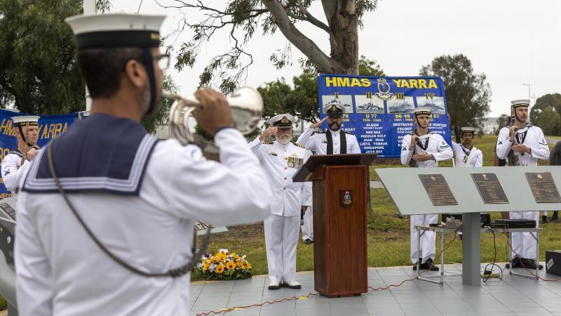 Commanding Officer HMAS Cerberus Captain Ainsley Morthorpe, centre, and Chaplain Matthew Campbell salute as Able Seaman Luke Glasson sounds the Last Post during the HMAS Yarra II commemorative service. Photo: Leading Seaman James McDougall
