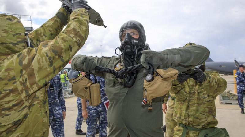 Aviators from No 381 and No. 1 Security Forces Squadrons guide a pilot with protective clothing through the decontamination processes during Exercise Toxic Safari at RAAF Base Amberley. Photo: Corporal Brett Sherriff