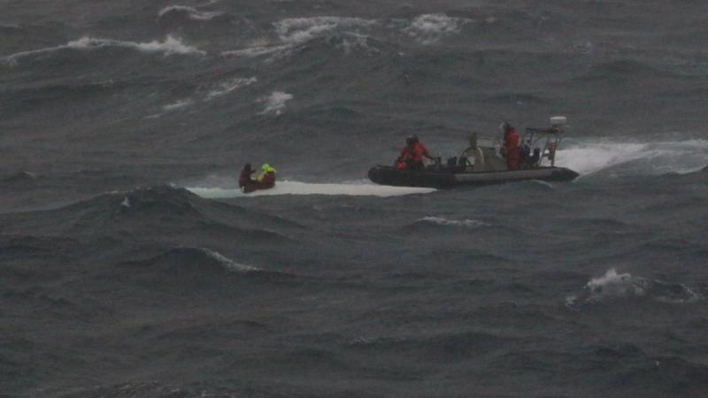 HMAS Brisbane’s rigid hulled inflatable boat crew rescues the stricken mariners from the hull of their upturned yacht off the coast of Wollongong. Photo: Supplied