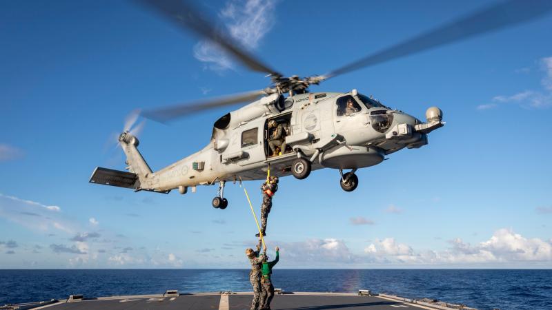 A Royal Australian Navy MH-60R Seahawk helicopter winches Commanding Officer HMAS Parramatta Commander David Murphy onto the flight deck during their regional presence deployment. Photo: Leading Seaman Leo Baumgartner