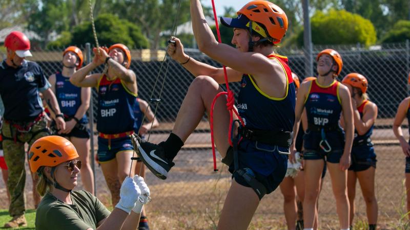 An AFLW Adelaide Crows player climbs a rope ladder with Army Sapper Abbey Patzel holding it steady during their visit to Robertson Barracks as part of their pre-season training camp. Photo: Captain Peter March