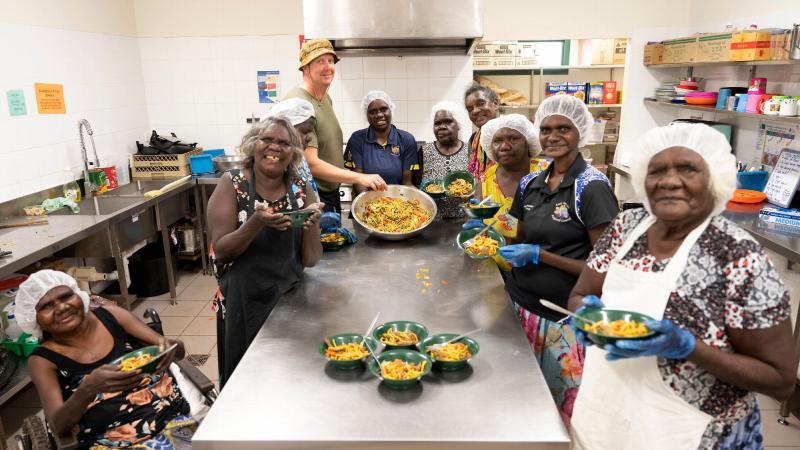 Army soldier Sergeant Nathan Judd with Gapuwiyak community members enjoying the meal they cooked during hospitality training as part of the Army Aboriginal Community Assistance Program in Gapuwiyak, Northern Territory. Photo: Corporal Lucas Petersen