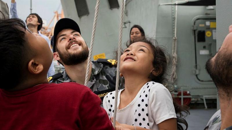Lieutenant Quaelan Brooks helps children from the Khlong Toey slum raise communication flags on HMAS Anzac during a port visit to Bangkok in 2018. Photo: Petty Officer Kayla Jackson
