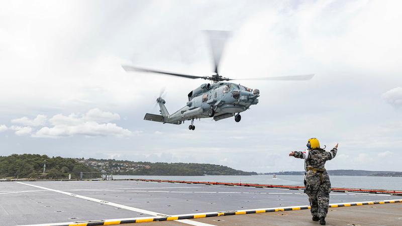 HMAS Choules' flight deck marshaller directs an MH-60R helicopter to the flight deck of HMAS Choules. Photo: Able Seaman jasmine Moody