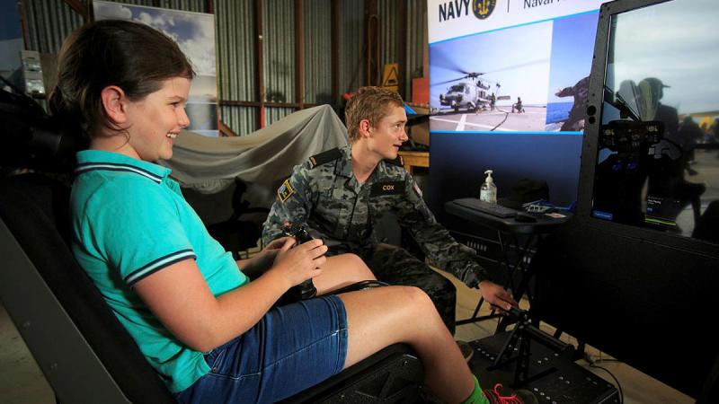 Seaman Liam Cox from HMAS Albatross guides 8-year-old Kira on the Navy helicopter simulator display at the Hunter Valley Airshow. Photo: Sergeant Glen McCarthy