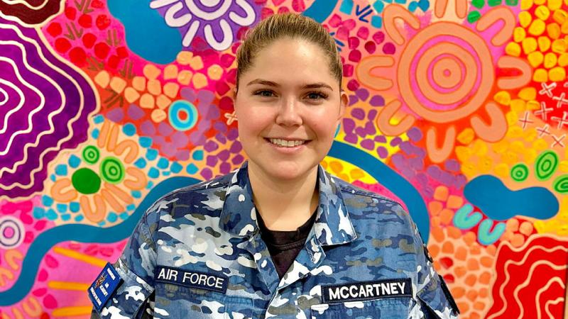 Flight Lieutenant Aimee McCartney stands before her painting titled ‘Nawu’ - one of the many traditional artworks now on display at her first solo exhibition in Melbourne.