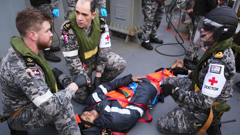 Leading Seaman Ryan Feenan, Leading Seaman Aaron Evans, and medical officer Lieutenant Jarrad Blackburn provide care to an injured mariner aboard an oil tanker during a medical evacuation in the Southern Indian Ocean. Photo: Tyson Burraston