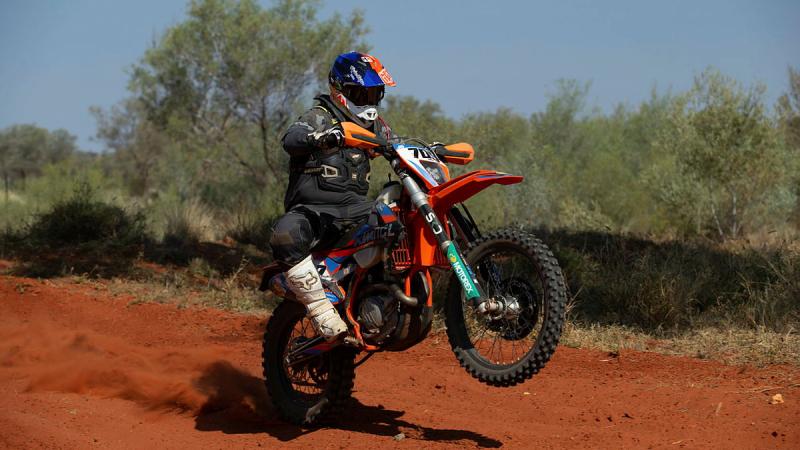 A person rides his dirt bike on red dirt in Alice Springs