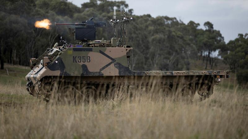 An Australian Army M113AS4 armoured logistics vehicle, fitted with optionally crewed combat vehicle technology and a remote weapon station, fires from a support-by-fire position during a human-machine team exercise.