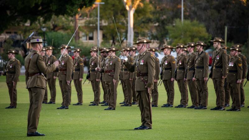 Australian Army officers and soldiers salute with swords during a parade