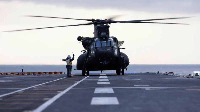 A Royal Australian Navy aviation support sailor marshals a United States Army MH-47G Chinook helicopter after landing on HMAS Adelaide during Exercise Balance Action. 