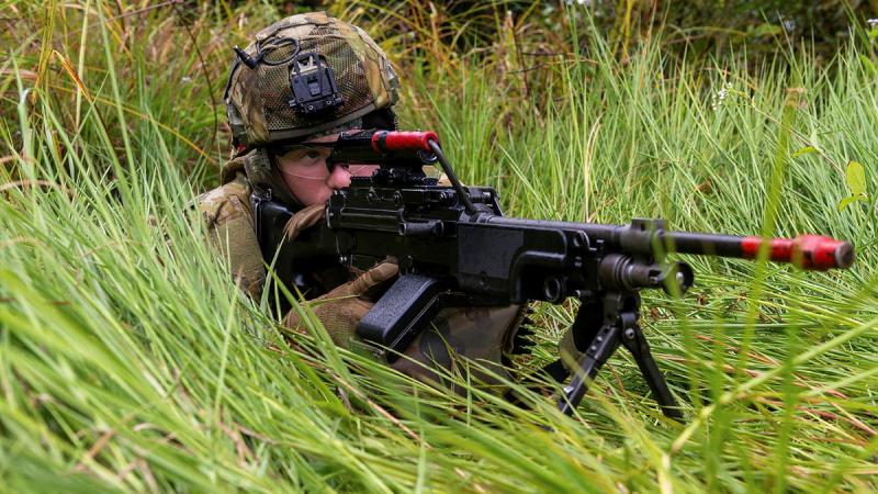 Solider lays in the grass with a machine gun.