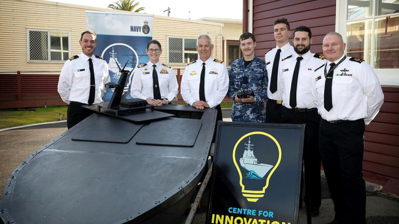 Aircraftman Max Tesoriero (centre) and project manager Sub Lieutenant Ben Jackson (far left) with senior Navy personnel and the uncrewed surface vessel, Lexcen, which he assisted in developing.