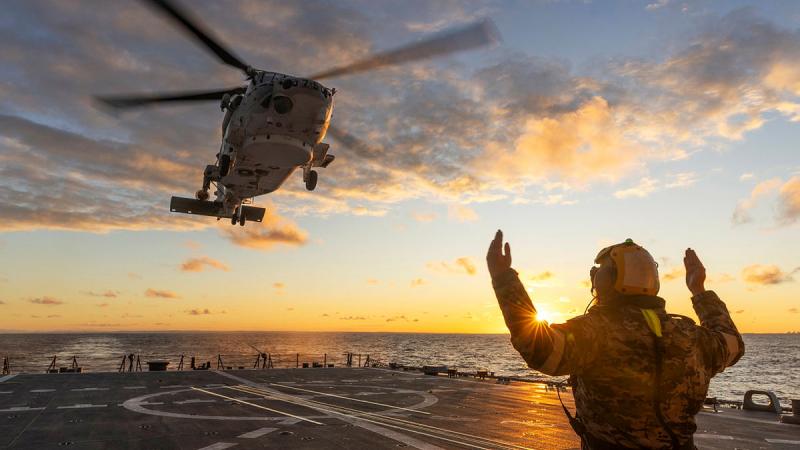 An Australian sailor marshals a Japanese helicopter to land on a ship during an exercise.