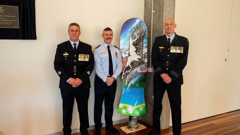 Pilot Officer Shane Collins stands with Commanding Officer, Officer Training School (OTS) Wing Commander Garth Herriot and OTS Squadron Warrant Officer, Warrant Officer Scott Robbins alongside the artwork Pilot Officer Shane Collins painted during his course.