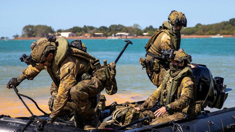 Army soldiers alight from a Zodiac on a beach.