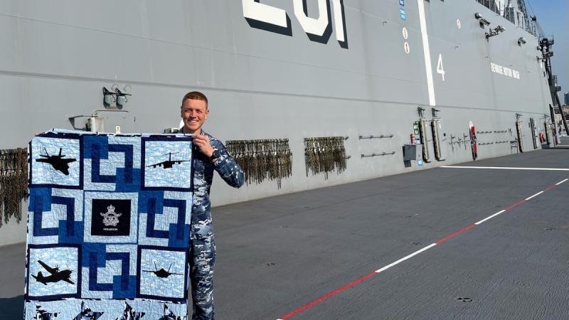 Air Traffic Controller, Flight Lieutenant Kristian Henderson proudly displays his Aussie Hero Quilt, received while deployed with HMAS Adelaide on Operation Tonga Assist 22.