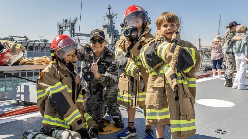 Leading Seaman Maritime Logistics Rebecca Signey with children in firefighting ensemble during HMAS Hobart’s Family Day, Fleet Base East, NSW. 