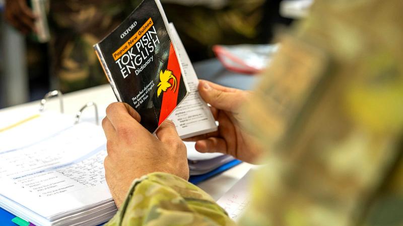An Australian Army special operations force soldier holding a Tok Pisin language book.