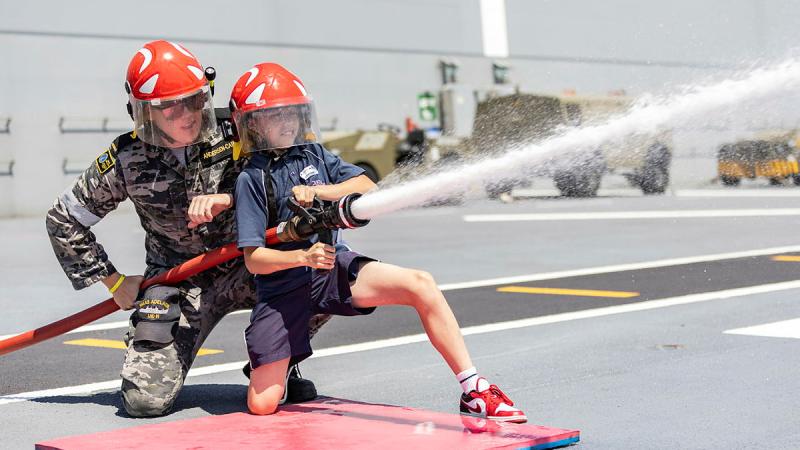 A HMAS Adelaide sailor helps a student from Navy Life Experience with fire hose operations during the inaugural Navy Life Expo in Sydney. Photos: Able Seaman Lucinda Allanson