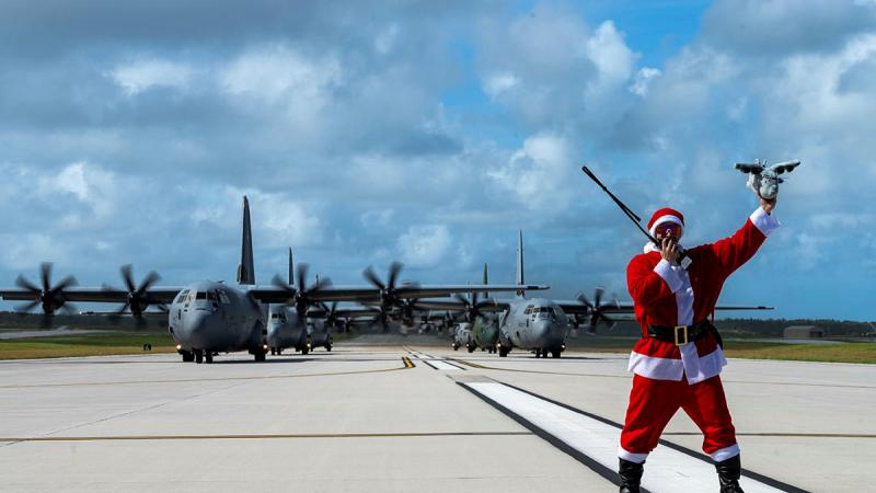USAF Major Zach “Santa Badger” Overbey stands before three USAF C-130J Super Hercules aircraft, a Royal Canadian Air Force C-130J Super Hercules, a Japan Air Self-Defense Force C-130H Hercules, 401st Tactical Airlift Squadron and a Republic of Korea Air Force C-130H Hercules, 251st Airlift Squadron during Operation Christmas Drop 2023. 