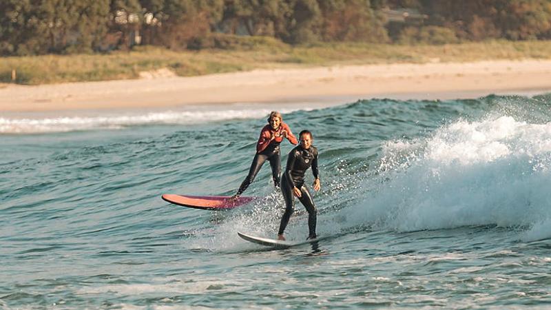Petty Officer Hannah Stiles and Pam Burridge ride a wave during the ADF Women’s Surf Development Camp in Ulladulla. 