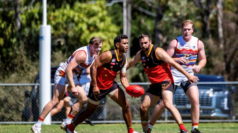 A Fitzroy Stars player lines up a hand pass as players chase him from the 4th Brigade AFL team at the Sir Douglas Nicholls Oval, Melbourne, March 2024. 